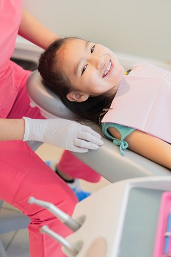 A vertical closeup of a little girl receiving dental treatment.