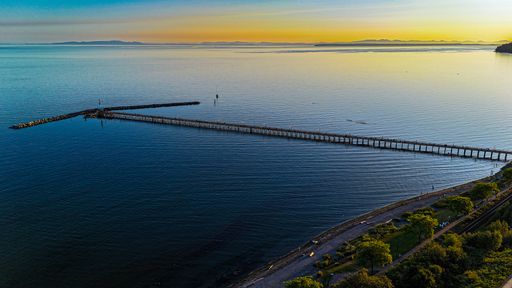 A serene drone view of White Rock Pier extending into calm waters during a stunning sunset in White Rock, Canada