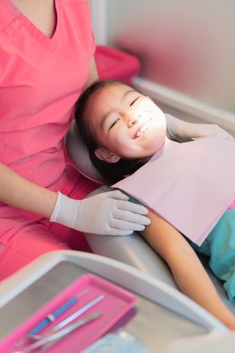 A vertical closeup of a little girl receiving dental treatment.
