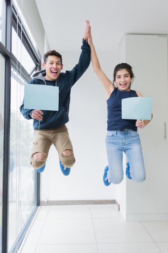 A vertical shot of a young man and a girl jumping and holding posters.