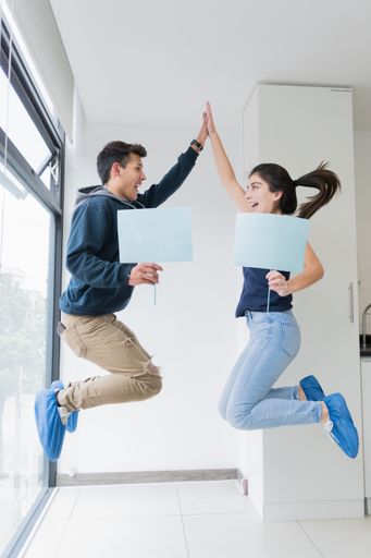 A vertical shot of a young man and a girl jumping and holding posters.