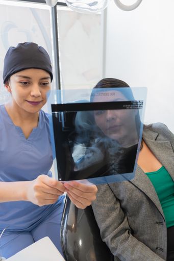 A vertical shot of a young female dentist checking x-ray of a patient.