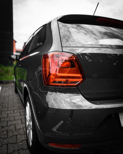 A vertical shot of a black shiny car parked in a car park with the gloomy sky reflecting in the window