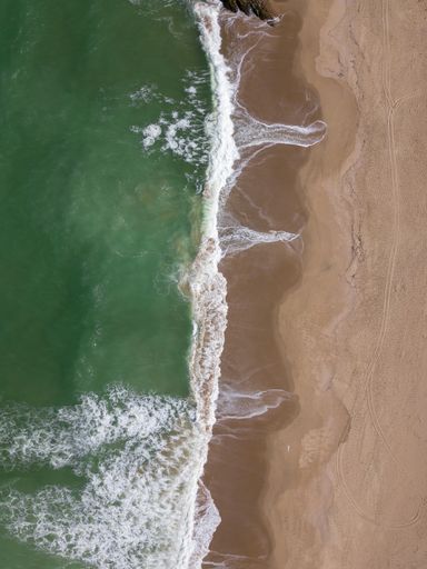 An aerial view of the sea waves washing the sandy shore