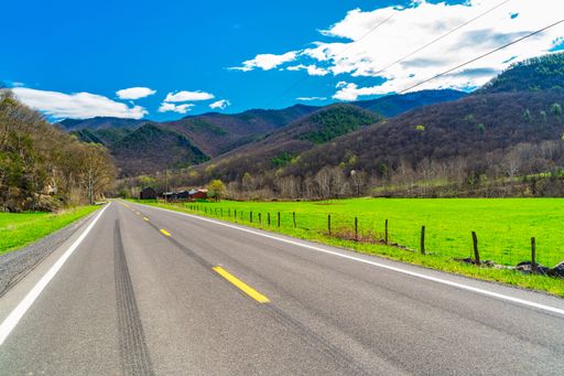 Scenic rural road with green fields and mountains under a bright blue sky on a sunny day in rural West Virginia.