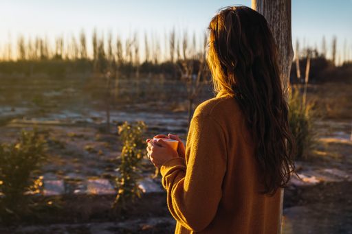A shot of the Latin woman from the back, drinking tea and watching the sunset.
