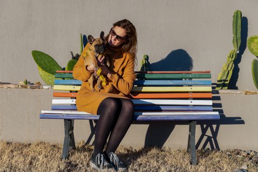 A shot of the Latin woman with a dog on a wooden bench outdoors.