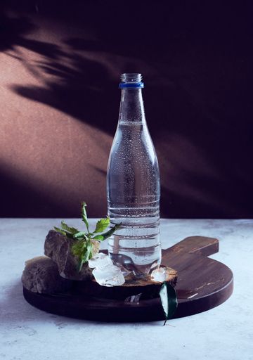 A vertical shot of a bottle of water on a wooden surface with stones and a twig