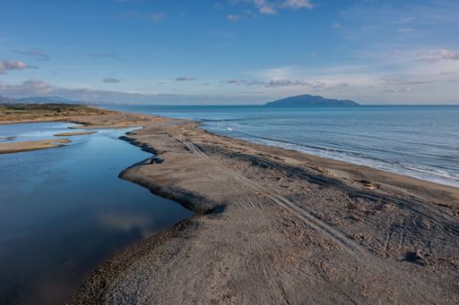 A serene coastal landscape with a sandy beach and calm ocean waters under a clear blue sky. the Otaki river mouth with estuary,