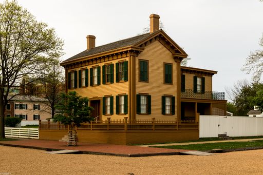 A historic yellow wooden house with green shutters and a picket fence in a quaint neighborhood.