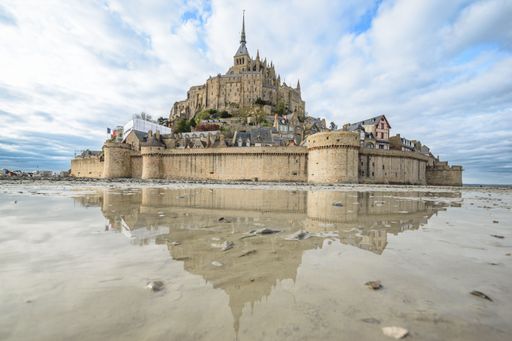 A stunning view of Mont Saint-Michel reflecting in the water during low tide under a cloudy sky