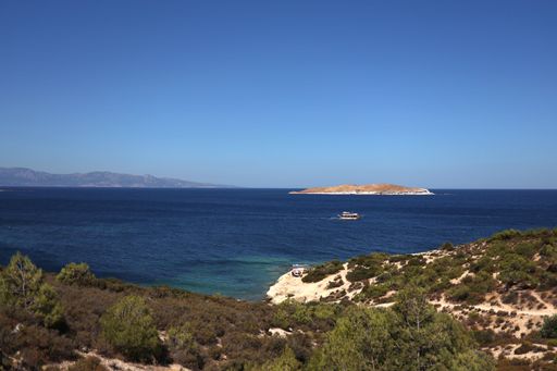 A scenic view of a coastal landscape with clear blue waters, a small island, and a boat sailing under a bright blue sky.