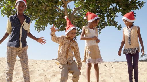 Happy Indian female and male kids celebrating New Year in Santa Claus hats on a beach
