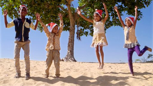 Happy Indian female and male kids celebrating New Year in Santa Claus hats on a beach