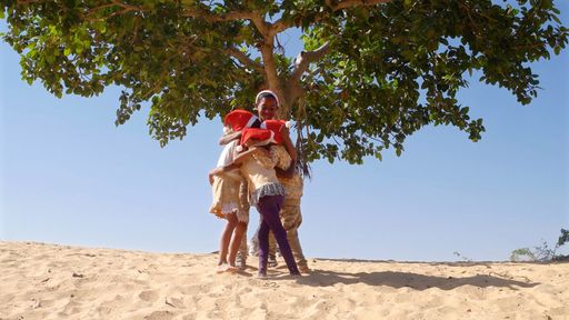 Happy Indian female and male kids celebrating New Year in Santa Claus hats on a beach