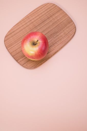 A vertical shot of fresh apple on a wooden board isolated on a pink background with copyspace