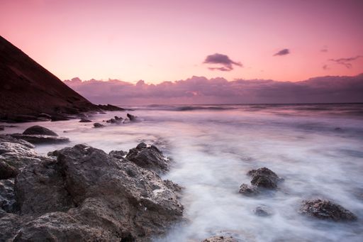 A mesmerizing view of the purple sky over the sea and cliffs at sunset