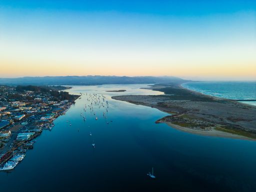 Aerial view of Morro Bay harbor with boats, cityscape, and coastline at sunset, California.