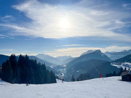A stunning winter landscape of a snow-covered mountain range with skiers and a clear blue sky.