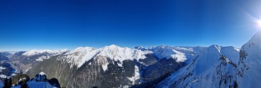 A panoramic view of snow-covered mountains under a clear blue sky with the sun shining brightly