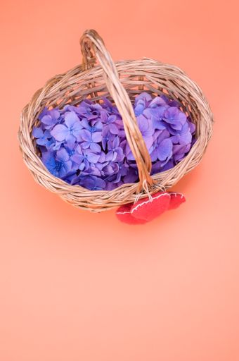 A vertical shot of purple hydrangea flowers with heart-shaped objects on a woven basket