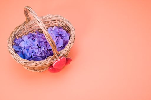 A vertical shot of purple hydrangea flowers with heart-shaped objects on a woven basket
