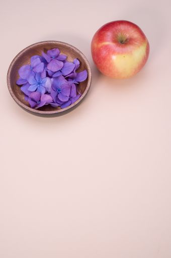 A bowl of fresh hydrangea flowers and an apple isolated on a pink background with free space for text