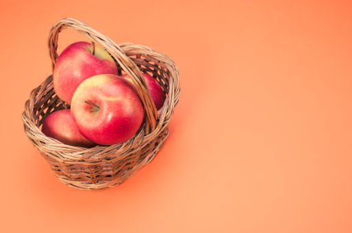 A closeup shot of fresh apples on a woven basket isolated on a pink background with copyspace