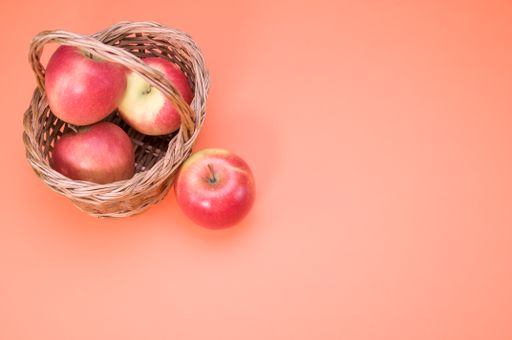 A basket of red apples isolated on a peach background with free space for text