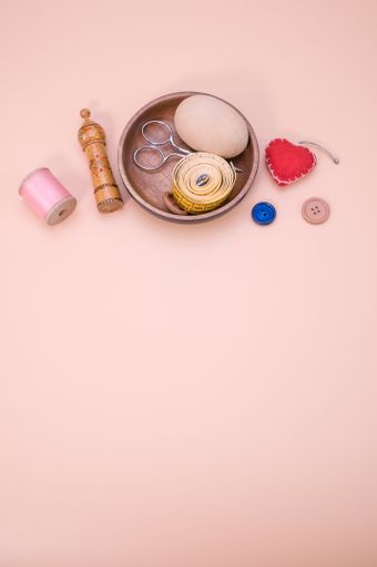 A vertical shot of stitching materials on a wooden bowl isolated on a pink background