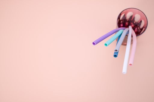 A closeup shot of colorful reusable bend straws in a glass isolated on pink background