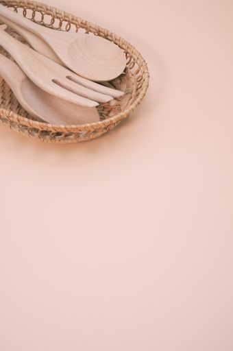 A vertical shot of wooden spoons and a fork on a woven basket isolated on pink background