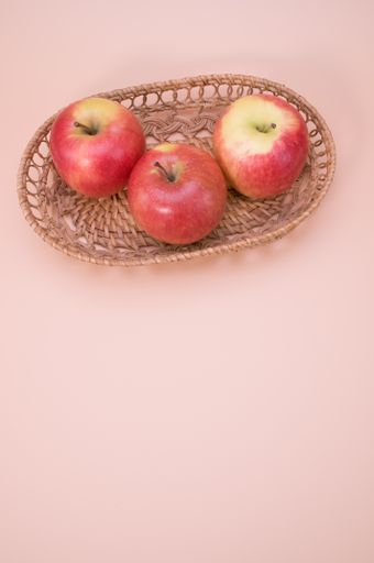 A vertical of fresh apples on a woven tray isolated on a pink background with copyspace
