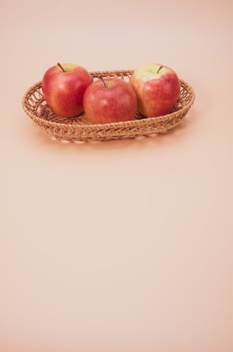 A vertical of fresh apples on a woven tray isolated on a pink background with copyspace