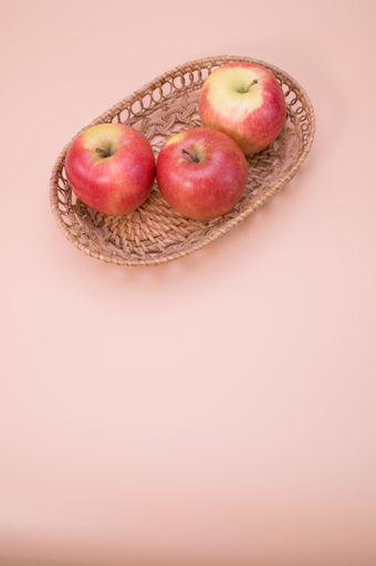 A vertical shot of fresh apples on a woven tray isolated on pink background with copyspace