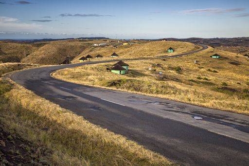 A beautiful shot of a curvy road with small houses on the sides and a blue sky in the background