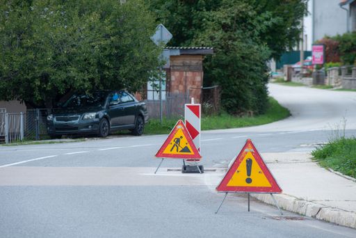 The road construction with public works and traffic signs on an empty street with trees and car parked in the background