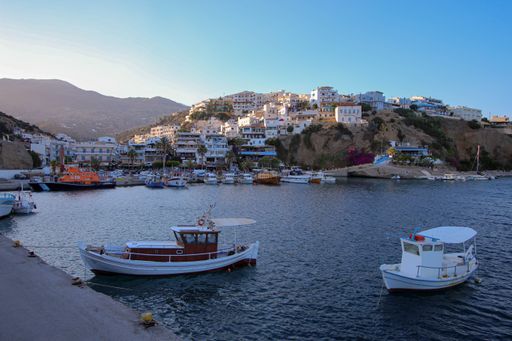 A tranquil scene of small boats in the harbor of Agia Galini with cliff buildings in the background under blue sky