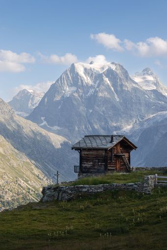 Summer landscape view of a typical Swiss chalet in front of the snow-capped Mont Collon mountain peak.