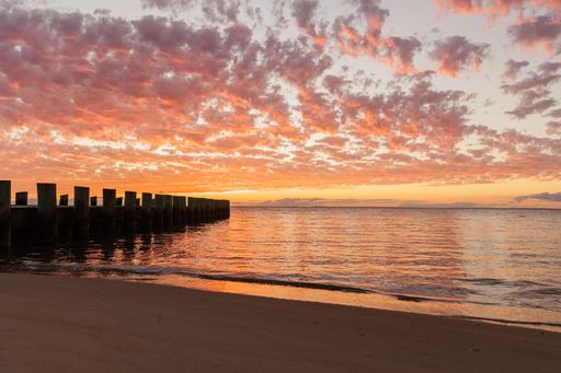 A beautiful sunset over a calm ocean with a pier extending into the water, and a sandy beach in the foreground.