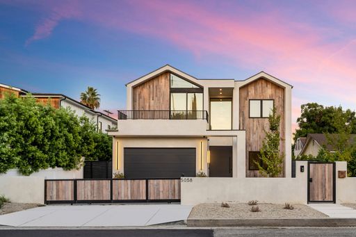 Modern two-story house with wooden accents and a beautiful sunset sky in the background.