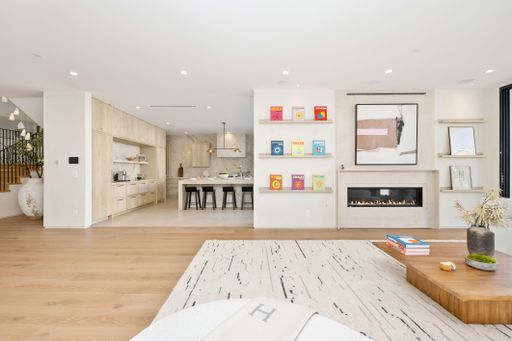 Modern open-concept living room and kitchen with minimalist design, featuring a fireplace, wooden floors, and contemporary decor.
