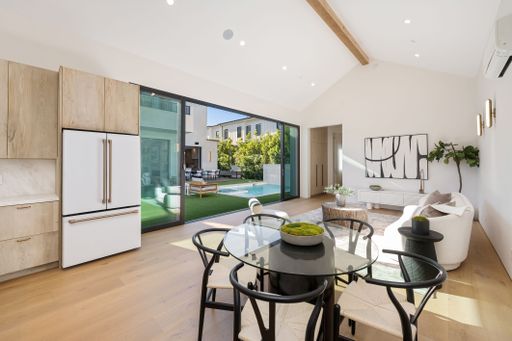 Modern open-plan living room and kitchen with large sliding doors opening to a patio and pool area, featuring minimalist decor and natural light.