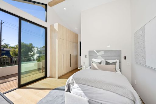 Modern bedroom with large windows, wooden flooring, and minimalist decor, featuring a comfortable bed and built-in wardrobe.