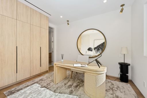Modern home office with a minimalist design, featuring a wooden desk, round mirror, and ample storage space.
