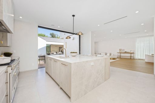 Modern open-concept kitchen featuring a large island, marble countertops, and a view of the living area and outdoor space.