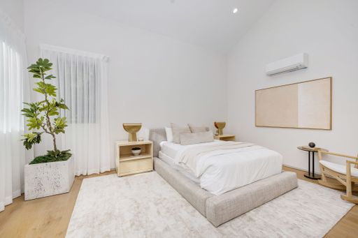 A modern minimalist bedroom with neutral tones, showcasing a large bed, indoor plant, and stylish decor.