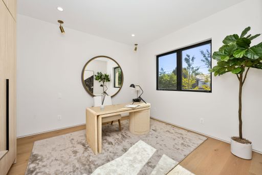 Minimalist home office with wooden desk, large round mirror, indoor plant, and natural light from a window.