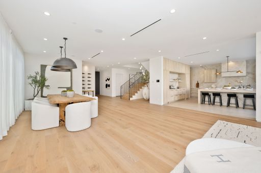 A modern open-plan living space with wooden flooring, dining area, and kitchen featuring minimalist decor and ample natural light.