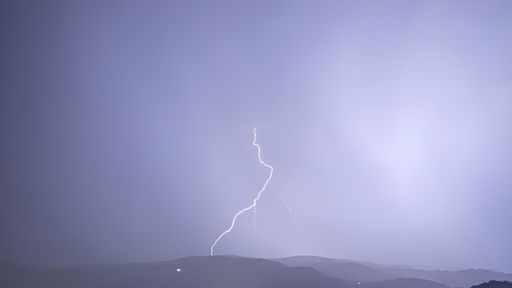 A striking lightning bolt captured over a mountain range during a stormy night.